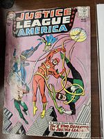 Front cover of Justice League of America #27 comic book showing multiple superheroes in action with a purple background