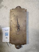 Rectangular metal hanging scale with embossed dial and pointer, showing numeric markings and text indicating weight and brand information.