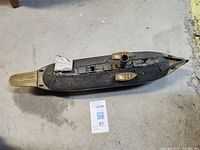 Full view of the wooden ship model placed on a concrete floor, showing the deck, rudder, and overall shape.