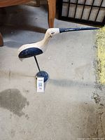 Full view of carved wooden bird sculpture standing on a concrete floor.