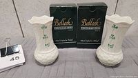Two white Belleek vases side by side with original boxes behind them. Each vase has hand-painted shamrocks on the body.
