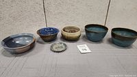 Full view of all five ceramic bowls and one small dish displayed in a row on a fabric-covered surface.