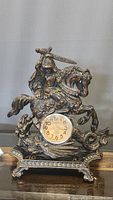 Full view of heavy metal clock showing knight on horse statue with raised sword and clock face embedded in base.