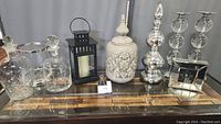 Photo showing the entire lot on table including ceramic jar with lid, crystal decanter and glasses, silver candlesticks, black metal lantern, and glass picture frame.