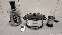 Lot of three appliances: Oster juicer, Hamilton Beach crock pot, Magic Bullet blender, arranged side by side on a table.