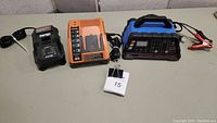 Full view of the three battery chargers Ryobi (black), Black & Decker (orange), and EverStart (blue/black) on a table