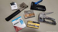 Photo of the lot showing three staplers and three packs of staples including Arrow, DeWalt, and T25 brands.