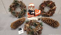 Full lot view showing the ceramic snowmobile figurine surrounded by three pine cone wreaths and two large pine cones