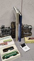 Photo shows vintage metal train bookends holding three hardcover railroad books with visible titles and two boxed collectible model cars in front.