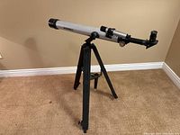 Full side view of silver and black Bushnell telescope mounted on black tripod on carpeted floor.
