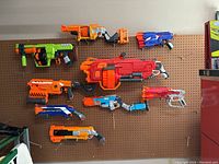 Nine Nerf blasters arranged on pegboard showing various styles and colors