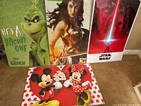 Four posters displayed vertically: The Grinch, Wonder Woman, Star Wars, and Mickey & Minnie Mouse, all new and sealed in plastic with cardboard backing.
