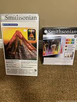 Front view of the unopened Smithsonian Giant Volcano and Magic Rocks science kits side-by-side showing brand and product names.