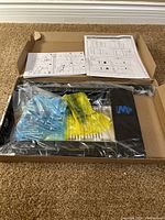 Box with TV wall mount parts, mounting hardware, and instruction sheets laid inside.