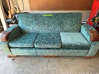Front view of green velvet sofa with three seat cushions and carved wooden armrests.