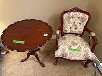 Full view of the vintage ornate side table with scalloped edges alongside the occasional chair with embroidered cushion upholstery.
