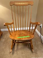 Front and angled front view of vintage wooden rocking chair with floral inlay on backrest and spindle spindles. Shows overall structure and condition.