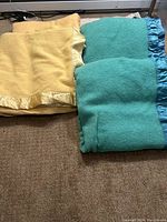 Wool blankets folded with satin trim visible, showing teal and yellow/beige colors.