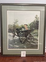 Full view of framed art showing the print of a baby and Labrador puppies in a wheelbarrow outdoors.