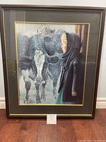 Framed art print showing the full image of the Amish girl and farm cows in snow scene, displayed on the floor against a wall.