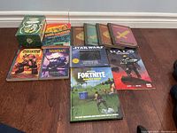 Overall assortment of books from Minecraft, Warcraft, Star Wars, Fortnite, and Halo titles laid out on a wood floor.