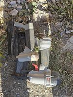 Two air tools placed on gravel: an air trimmer and an air stapler, showing side views with grips and air connectors