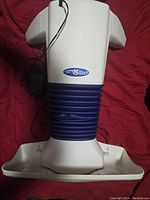 Top-down view of white and blue Back2Life back and hip massager with power adapter on red fabric background.