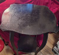 Top view of the black wooden table with scratches and wear visible on the scalloped top surface.