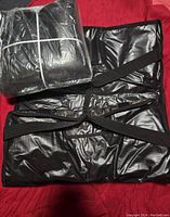 Two black insulated pizza delivery bags, one folded and still shrink-wrapped, and one laid open to show straps and padded interior.