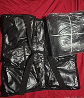 Two black large pizza bags, one unfolded and one in plastic wrap, showing straps, zipper and padded construction.
