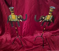 Pair of elephant-shaped candle holders showing front view with red cloth background