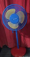 Front view of the Duracraft standing fan showing blue grill, yellow blades, and red base.