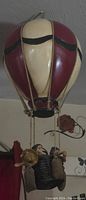Front view of the hanging hot air balloon decorative model showing cream and maroon balloon with black accents and a basket holding figurines below.