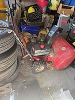 Left-side view showing red housing, black engine cover, front auger and treaded tire