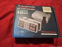 Front of the box showing the Mini Game Anniversary Edition entertainment system with a console and two controllers illustrated, highlighting 620 built-in classic games.