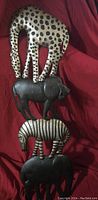 Metal hanging art showing four stacked safari animals against a burgundy fabric background.