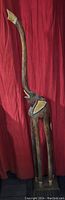 Front view of tall wooden elephant sculpture with elongated trunk and legs against red fabric background.