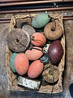 Basket with multiple wooden marine buoys and flotation discs in orange, green, burgundy colors, showing natural wear and weathering.