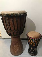 Side view of the pair of drums showing the large natural wood djembe and smaller painted drum