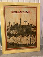 Full view of the framed 1968 Seattle poster illustrating the Seattle skyline with boats, the Space Needle, and other city landmarks in black and orange print, mounted on board within a light wood frame.