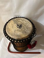 Top angled view of the drum showing natural skin drum head with Ethno logo and attached tension ropes with the stick lying next to it.