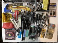 Photo showing a wide array of drill bits and accessories including packaged and loose items various sizes and types, laid out on a table.