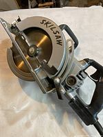 Angle view of the Skilsaw Model 77 showing the metal blade guard and the black handle grip with the Skilsaw logo visible on the blade guard.