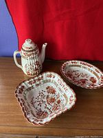 Spode India Tree coffee pot, square serving bowl, and round serving bowl displayed on wooden surface in front of red background