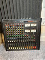 Front view of TASCAM M-208 mixer showing 8 input channels with colored knobs and volume faders.