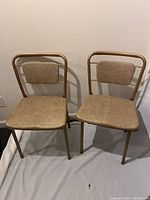 Front view of two vintage Cosco folding chairs with padded tan seats and backrests.