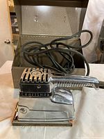 Full view of the Craftsman half-sheet sander with power cord coiled and original metal case in the background.