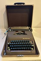 Front view of vintage Smith-Corona Clipper typewriter inside open hard case, showing keyboard, keys and upper carriage with ruler markings.