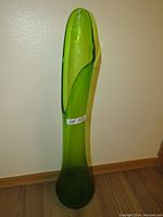 Tall lime green freeform glass sculpture against wall and wood floor