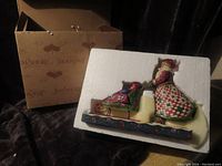 Jim Shore sculpture in original styrofoam packaging showing Santa pushing a sleigh styled like a baby stroller inside the box